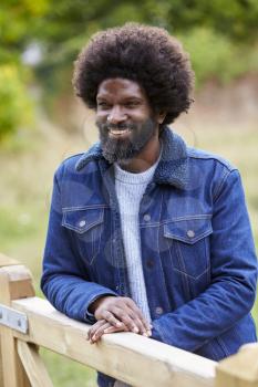 Happy adult black man leaning on a wooden fance in the countryside smiling, close up