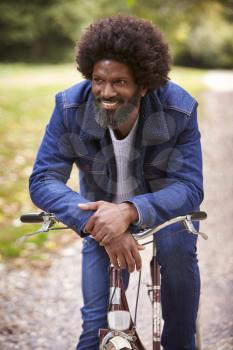 Black middle aged man sitting on a bike in  a park, leaning on the handlebars smiling, front view, close up