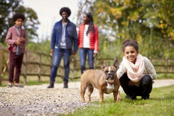 Mixed race girl squatting to pet her dog during a family walk in the countryside looking to camera, low angle