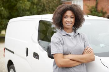 Young black female tradesperson standing next to her white van with arms crossed, close up