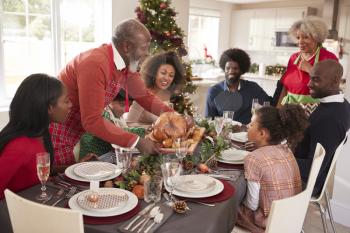 Grandfather bringing the roast turkey to the dinner table during a multi generation, mixed race family Christmas celebration, elevated view