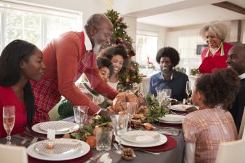 Grandfather bringing the roast turkey to the dinner table during a multi generation, mixed race family Christmas celebration, close up