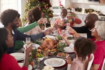 Multi generation mixed race family pouring champagne and raising glasses to make a toast sitting at the Christmas dinner table, elevated view