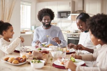 Happy mixed race young family of four eating Sunday dinner together, front view