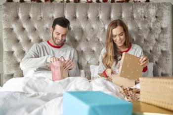 Front View Of Couple In Bed At Home Opening Gifts On Christmas Day