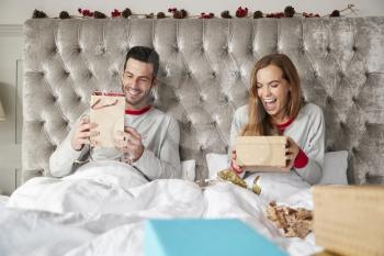 Front View Of Couple In Bed At Home Opening Gifts On Christmas Day
