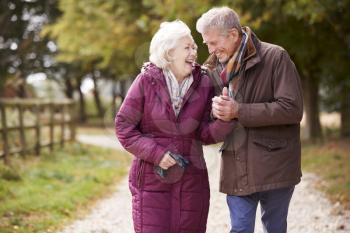 Active Senior Couple On Autumn Walk On Path Through Countryside