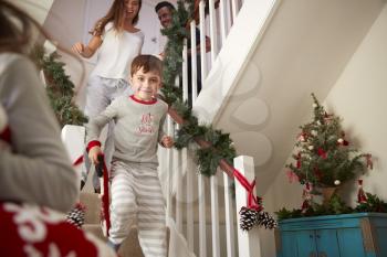 Excited Family Wearing Pajamas Running Down Stairs Holding Stockings On Christmas Morning