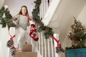 Excited Girl Wearing Pajamas Running Down Stairs Holding Stockings On Christmas Morning