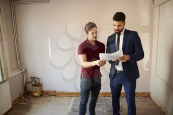 Male First Time Buyer Looking At House Survey With Realtor