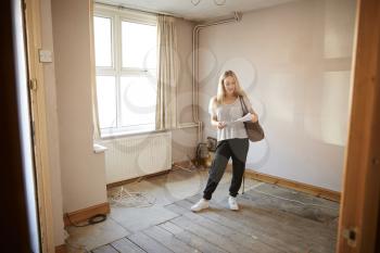 Female First Time Buyer Looking At House Survey In Room To Be Renovated