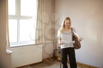 Female First Time Buyer Looking At House Survey In Room To Be Renovated