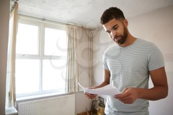 Male First Time Buyer Looking At House Survey In Room To Be Renovated
