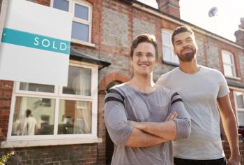 Portrait Of Two Men Standing Outside New Home With Sold Sign