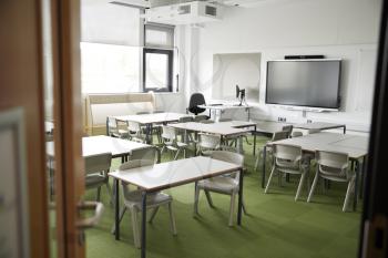 An empty classroom in a primary school with white desks and chairs, seen from doorway