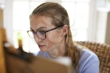 Female Teenage Artist Sitting At Easel Drawing Picture