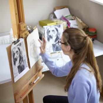 Female Teenage Artist Sitting At Easel Drawing Picture Of Dog From Photograph In Charcoal