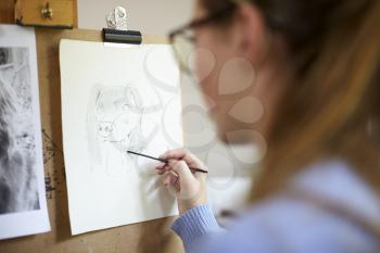 Close Up Of Female Teenage Artist Sitting At Easel Drawing Picture Of Dog From Photograph In Charcoal