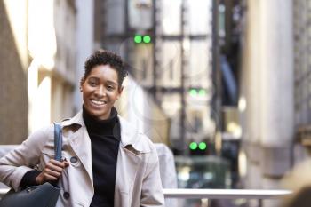 Close up of a millennial black businesswoman standing on a street in London smiling to camera, waist up