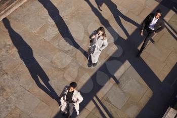 Aerial view of three business people walking in the same direction on a sunny urban street, horizontal
