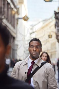 Young black businessman walking in a busy London street looking ahead, close up, vertical