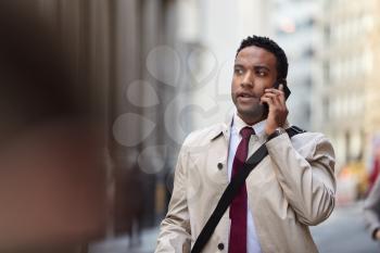 Millennial black businessman walking in a busy London street using smartphone, close up