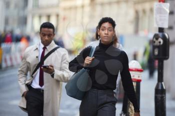 Young black woman walking in a London street carrying handbag, front view