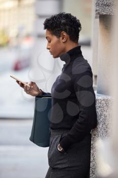 Young black woman standing on a street in London using her smartphone, side view, close up, vertical