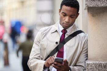 Young black businessman leaning on a wall in the street in London using smartphone, selective focus, close up