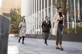 Three millennial city workers walking in the street, low angle, full length