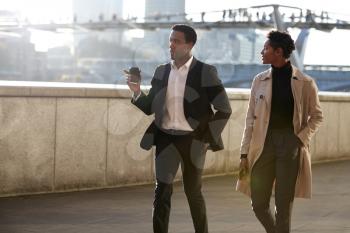 Two business colleagues walking by the Thames riverside in the city of London talking, man gesturing