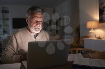 Senior Hispanic man checking his finances online at home using a laptop computer at night