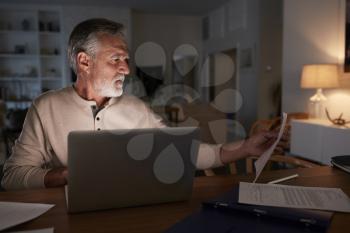 Senior Hispanic man checking his finances online at home using a laptop computer at night