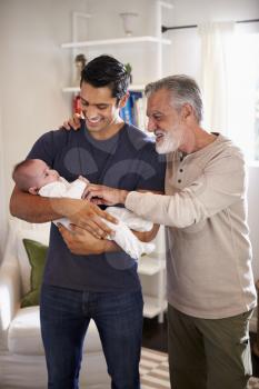 Proud senior Hispanic man standing with his adult son holding his four month old boy, vertical