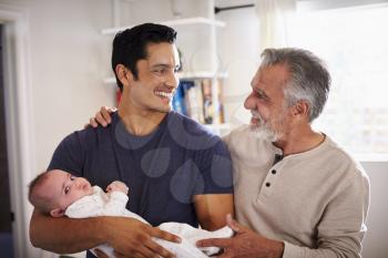 Proud senior Hispanic man standing with his adult son holding his four month old boy
