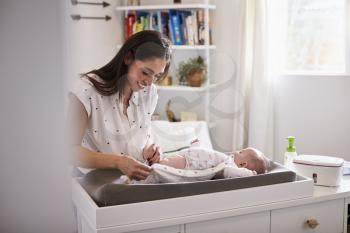 Happy mother changing the diaper of her newborn son at home on changing table, selective focus
