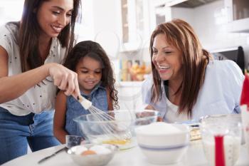 Young girl making a cake in the kitchen with her mum and grandmother, close up