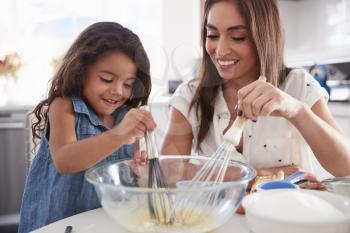 Young Hispanic girl making cake mix in the kitchen with her mum, close up