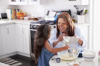 Young Hispanic girl making cake in the kitchen with her grandma, looking at each other