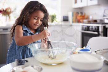 Young Hispanic girl making a cake in the kitchen on her own, close up