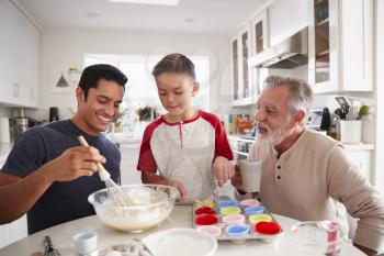 Three male generations of family preparing cakes together at the table in the kitchen, close up