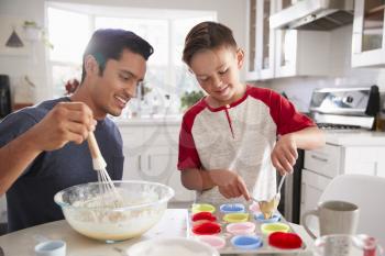 Pre-teen boy standing at the table in the kitchen making cakes with his father, close up