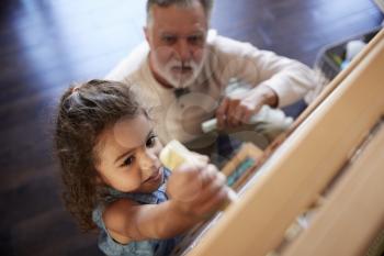 Senior man sitting on the floor watching his granddaughter drawing on a blackboard, elevated view
