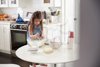 Young girl in the kitchen mixing cake mixture on her own, front view