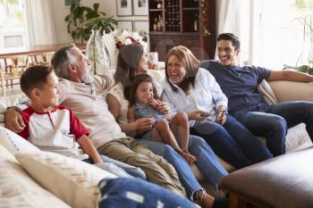 Three generation Hispanic family sitting on the sofa watching TV, grandmother using remote control