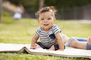 Little baby boy sitting up on a blanket in the park looking to camera, close up