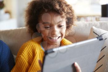 Portrait of pre-teen girl looking at tablet computer screen laughing, close up, selective focus