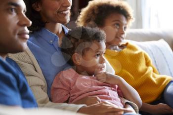Close up of children sitting on the sofa in their living room watching TV with their parents, side view