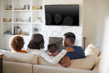 Back view of young family sitting on the sofa and watching TV together in their living room, close up