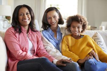 Three generation family female family group sitting on a sofa in the living room smiling to camera, close up